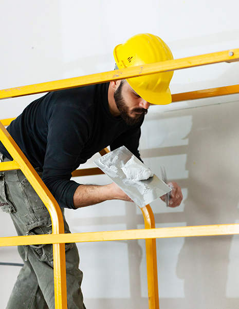 San Marcos Drywall Repair man standing on  scaffolding applying joint compound to a putty knife